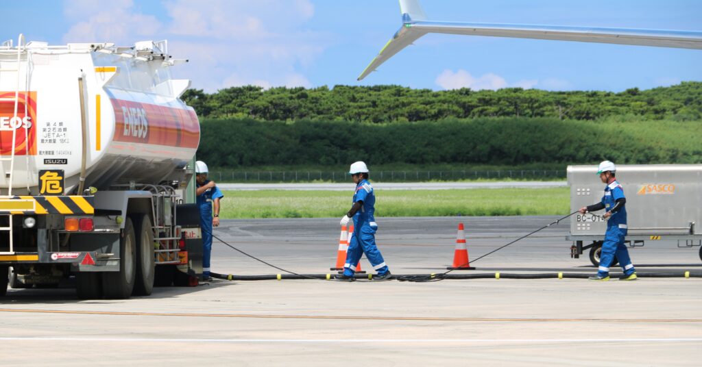 給油車両と航空機の間で給油ホースを扱う作業員